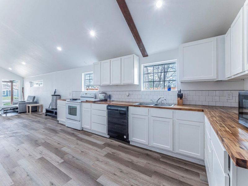 Kitchen featuring lofted ceiling with beams, wood counters, electric range, dishwasher, and white cabinetry