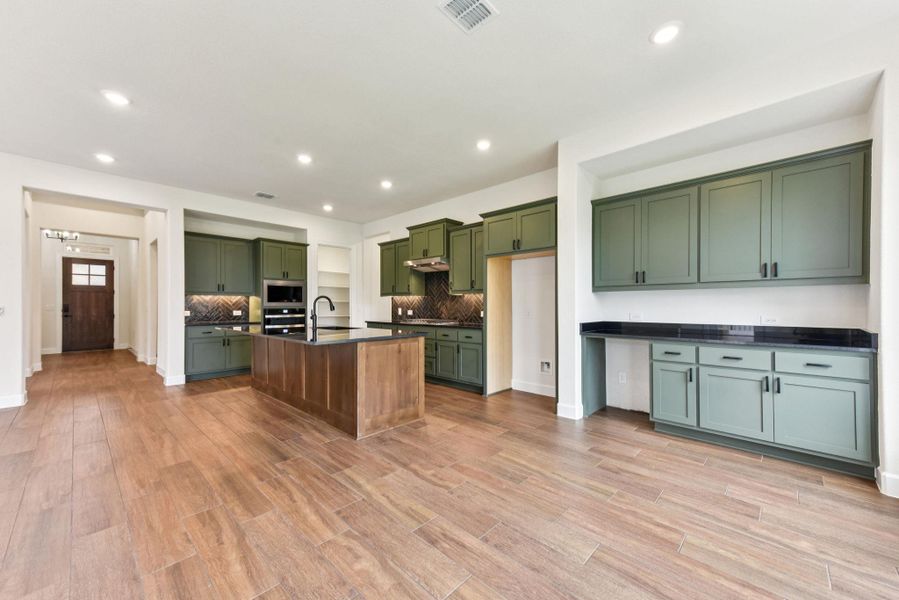 Kitchen featuring green cabinetry, a center island with sink, recessed lighting, backsplash, and light wood-style flooring