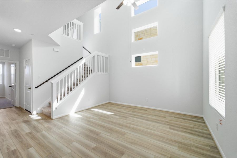 Unfurnished living room with a ceiling fan, light wood finished floors, and a high ceiling