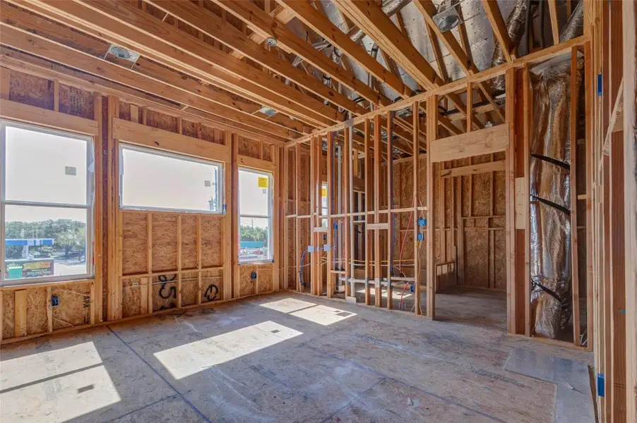 Spacious framed room with large windows, vaulted ceiling lines, and visible HVAC and electrical systems overhead. This construction-stage view highlights the scale, light, and future livability of the space, offering a strong sense of how the finished room will feel once drywall, flooring, and finishes are complete. Spacious framed room with large windows, vaulted ceiling lines, and visible HVAC and electrical systems overhead. This construction-stage view highlights the scale, light, and future livability of the space, offering a strong sense of how the finished room will feel once drywall, flooring, and finishes are complete.