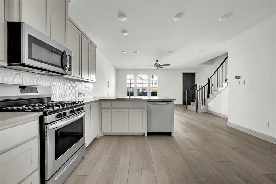 Kitchen featuring stainless steel appliances, a peninsula, light wood-style flooring, tasteful backsplash, and open floor plan Kitchen featuring stainless steel appliances, a peninsula, light wood-style flooring, tasteful backsplash, and open floor plan