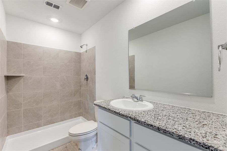 Bathroom featuring a tile shower, vanity, and toilet