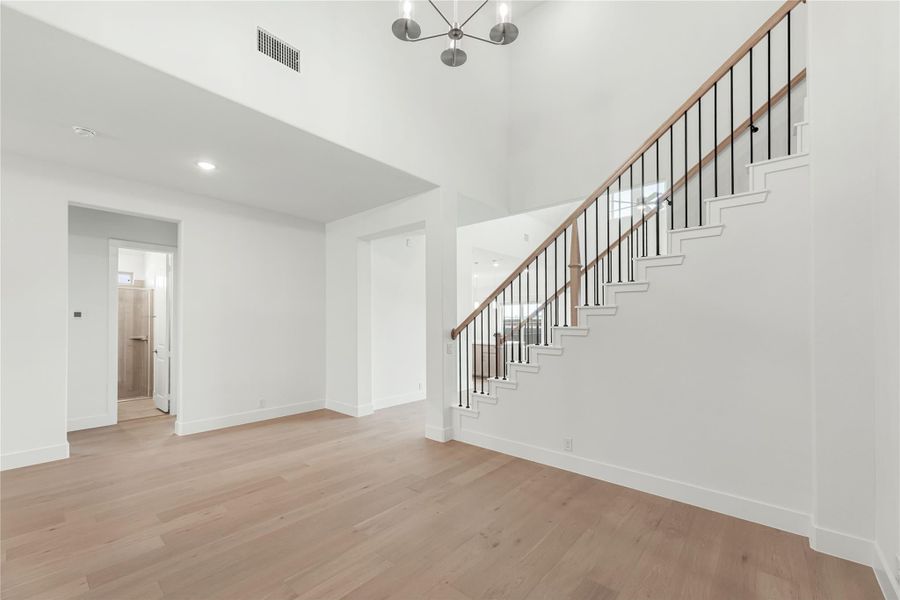 Open foyer with wood staircase, black iron balusters, light hardwood floors, and modern chandelier