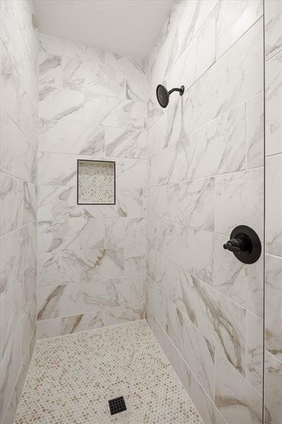 Tiled shower featuring large format white and grey veined wall tiles, a built-in recessed niche with mosaic tile, a matte black shower head, and a matte black shower control