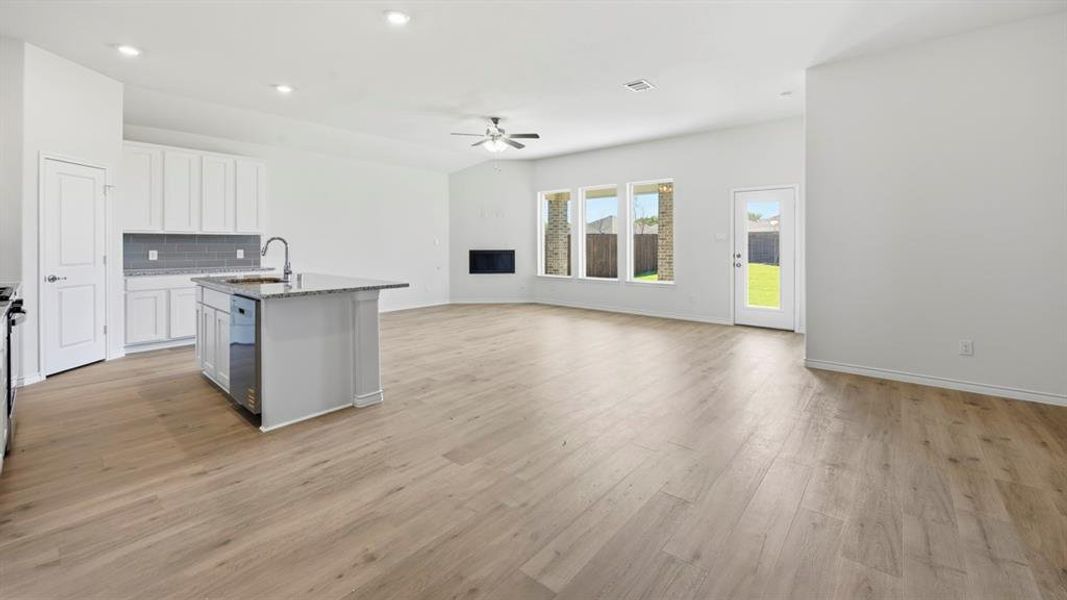 Kitchen featuring backsplash, a kitchen island with sink, light stone counters, open floor plan, and white cabinets