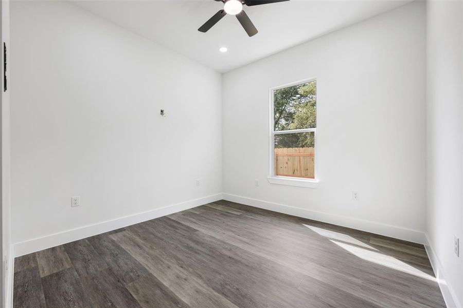Spacious room featuring wood-finish flooring, white walls, and a ceiling fan with integrated lighting