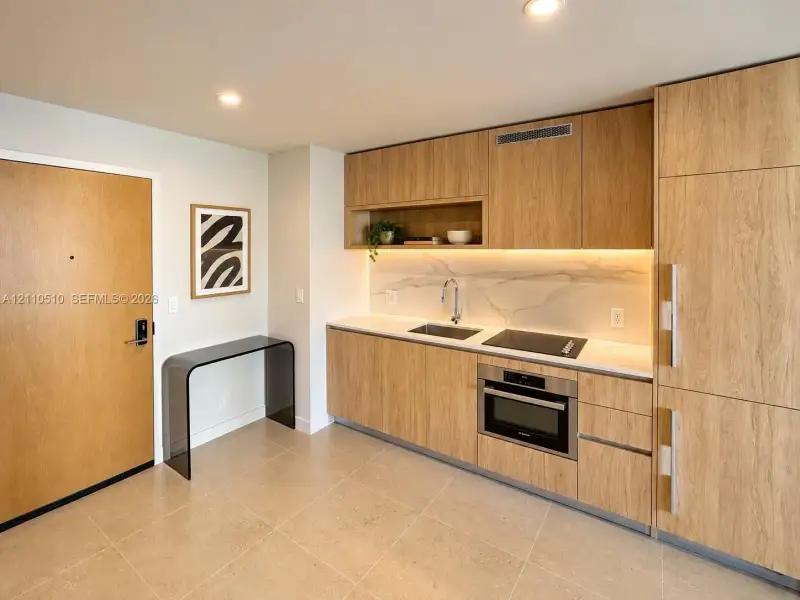 Kitchen featuring wood-finish cabinetry, stone-surface backsplash, integrated cooktop, built-in oven, and recessed lighting Kitchen featuring wood-finish cabinetry, stone-surface backsplash, integrated cooktop, built-in oven, and recessed lighting
