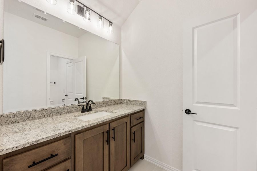 Bathroom vanity with granite countertop, wood cabinets, undermount sink, and large mirror with overhead lighting