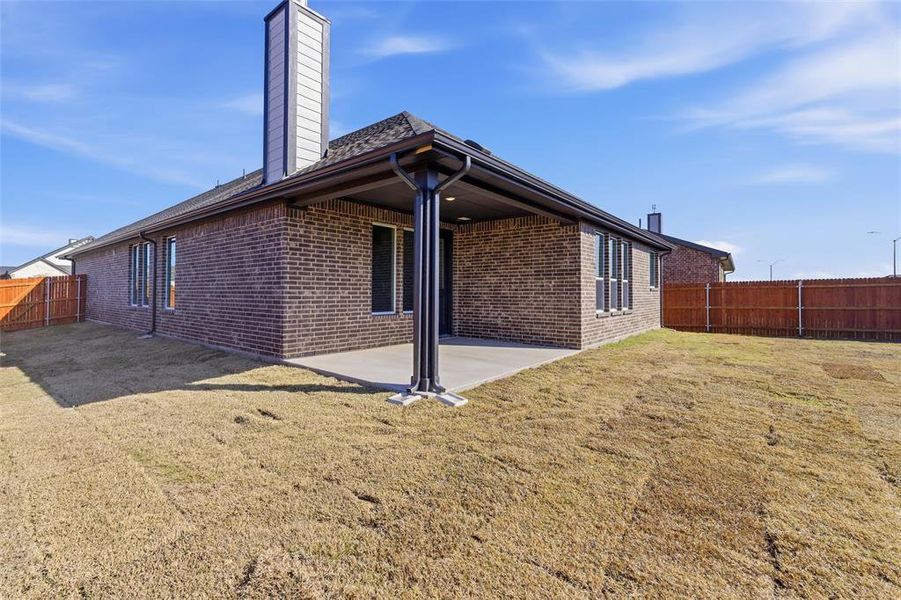 Rear view of house with a fenced backyard, a chimney, a patio, and brick siding