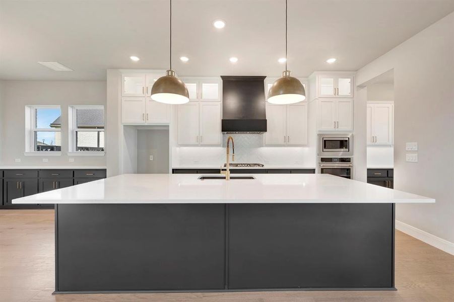 Two tone kitchen with dual tone cabinets, a large island, glass fronted cabinets, stainless steel appliances, and light stone countertops Two tone kitchen with dual tone cabinets, a large island, glass fronted cabinets, stainless steel appliances, and light stone countertops