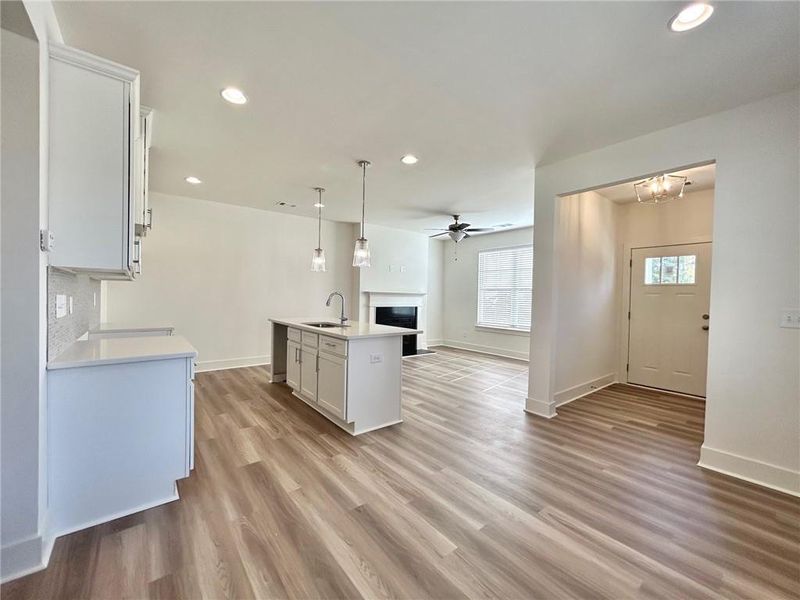 Kitchen with light wood-type flooring, hanging light fixtures, sink, and an island with sink