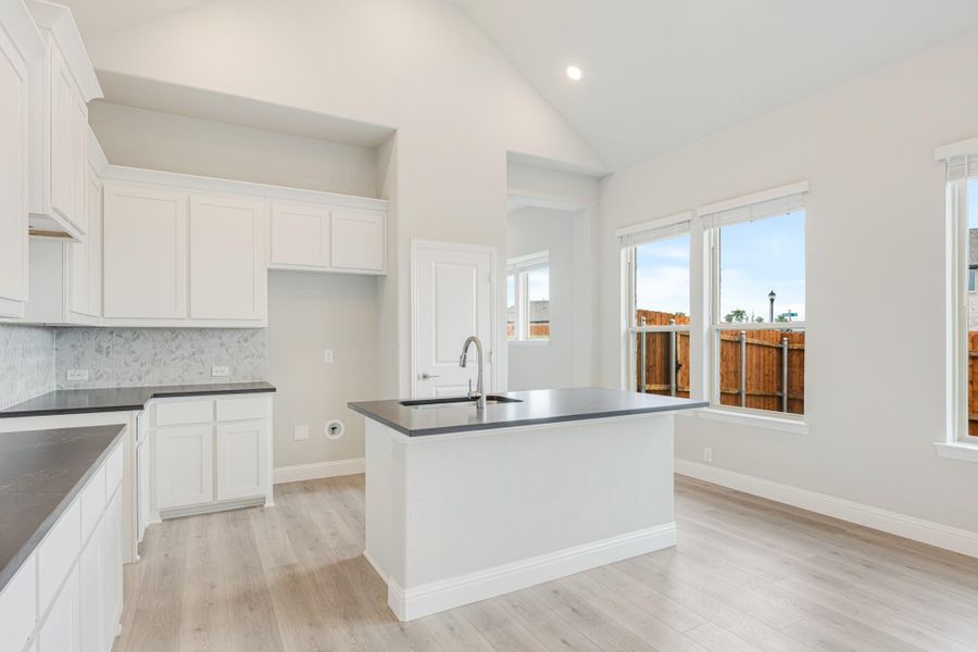 Kitchen with white cabinets, dark countertops, center island with sink, and light wood floors