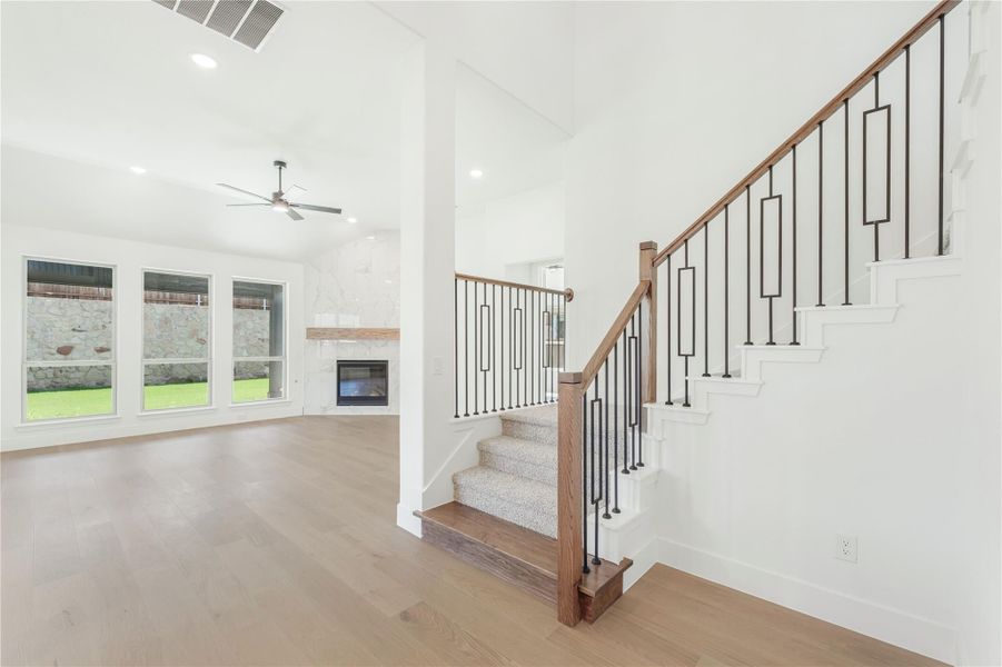 Open living area with wood staircase, iron balusters, hardwood floors, and stone fireplace in background Open living area with wood staircase, iron balusters, hardwood floors, and stone fireplace in background