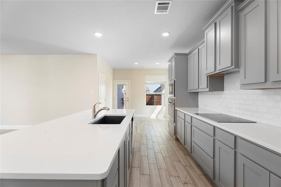 Kitchen featuring gray cabinets, decorative backsplash, a center island with sink, recessed lighting, and light countertops