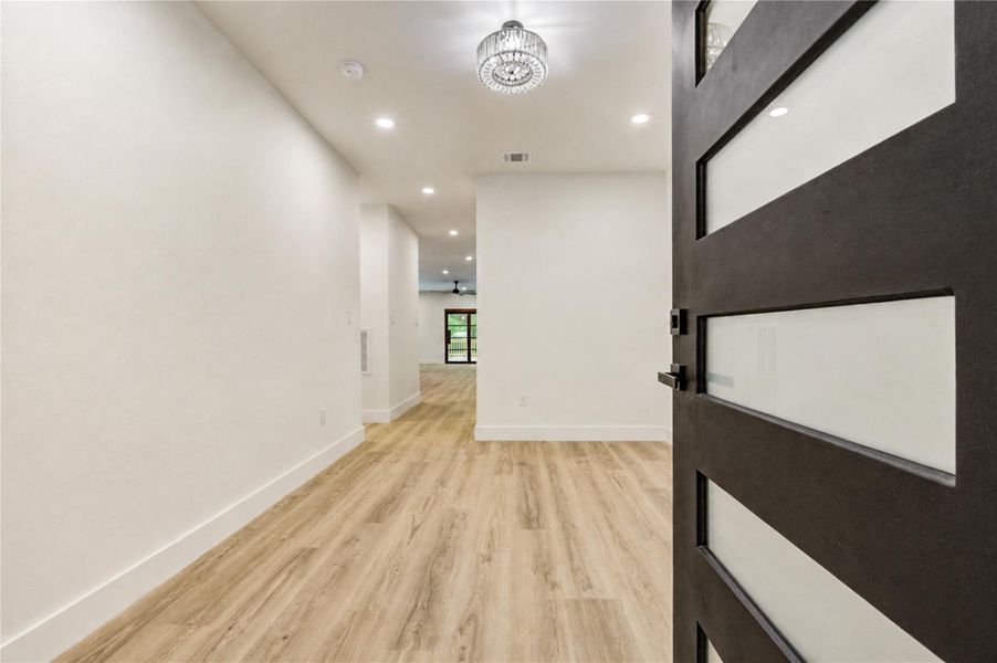 Step into a bright, open hallway featuring elegant LVP flooring and modern recessed lighting, leading to the heart of the home.
