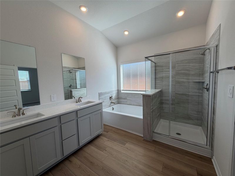 Bathroom featuring light wood-style floors, a bath, a shower stall, double vanity, and lofted ceiling Bathroom featuring light wood-style floors, a bath, a shower stall, double vanity, and lofted ceiling