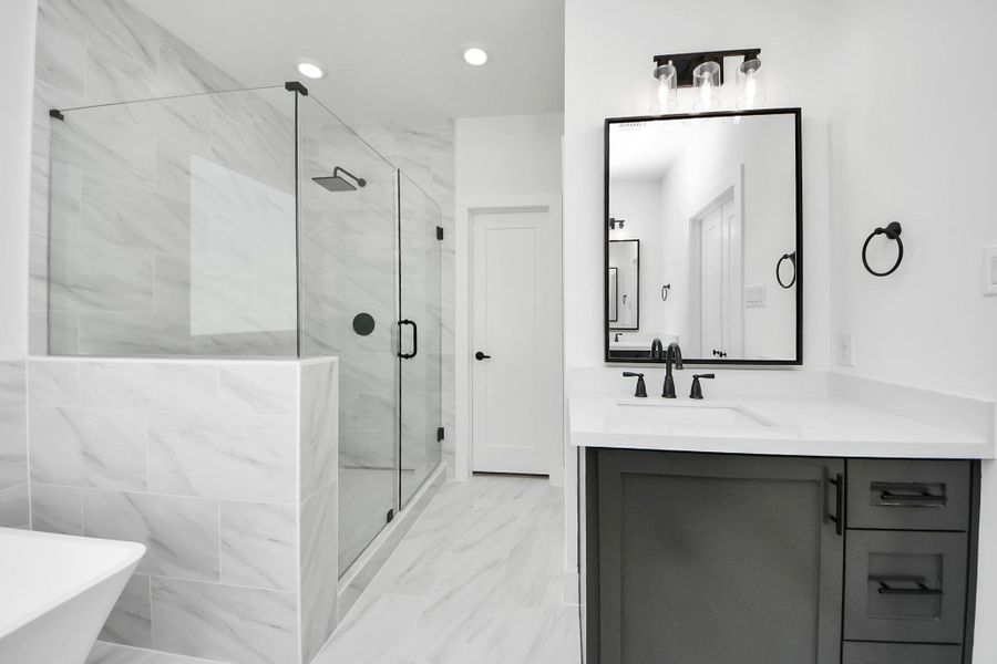 This bathroom features a modern design with a spacious glass-enclosed shower, large wall tiles, and a sleek vanity with a black-framed mirror. The neutral color palette and stylish fixtures create a clean, contemporary look. This bathroom features a modern design with a spacious glass-enclosed shower, large wall tiles, and a sleek vanity with a black-framed mirror. The neutral color palette and stylish fixtures create a clean, contemporary look.