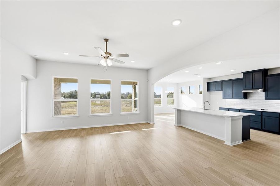 Kitchen featuring arched walkways, a center island with sink, backsplash, light wood-style flooring, and a ceiling fan