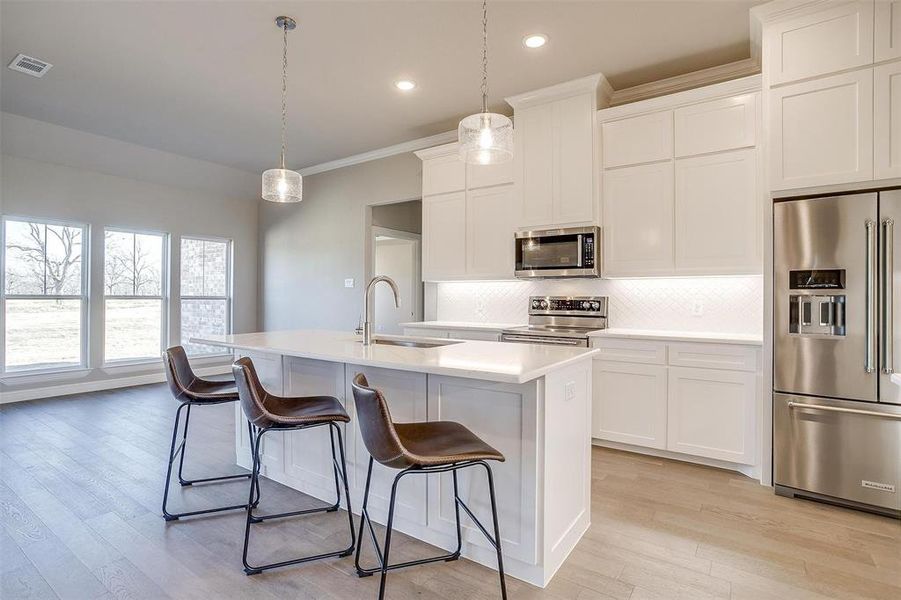 Kitchen with sink, decorative light fixtures, a center island with sink, stainless steel appliances, and white cabinets