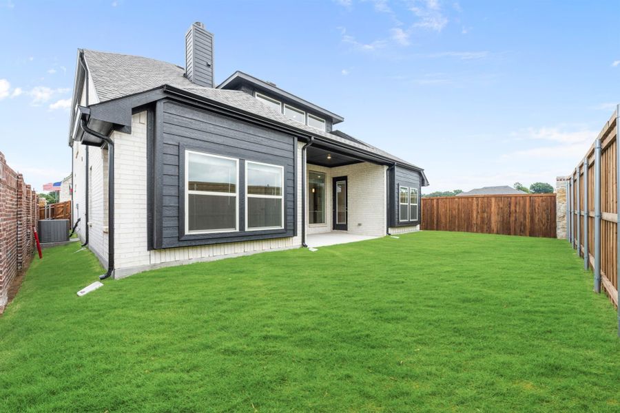 Home's rear exterior with dark siding, brick accents, covered patio, and fenced backyard with green lawn
