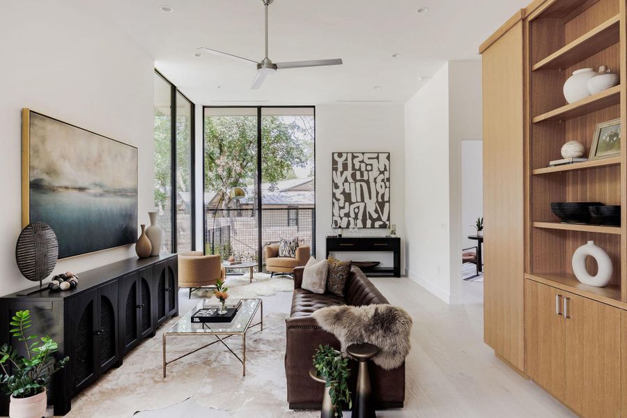 Living room featuring expansive windows, built in features, a ceiling fan, and light wood-style floors Living room featuring expansive windows, built in features, a ceiling fan, and light wood-style floors