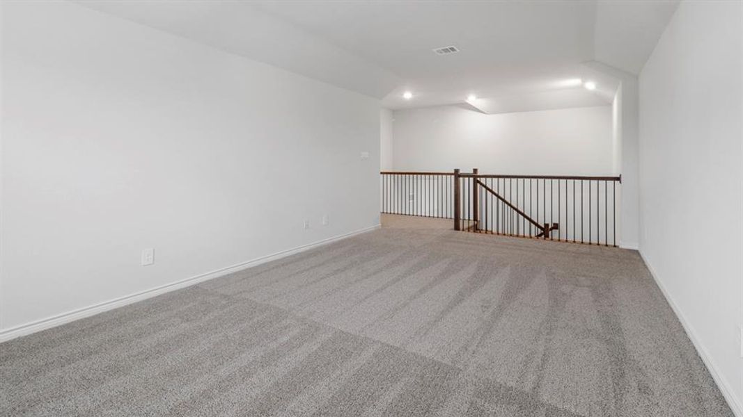 Spacious upper-level room featuring light gray carpeting, white walls, and a dark metal baluster railing