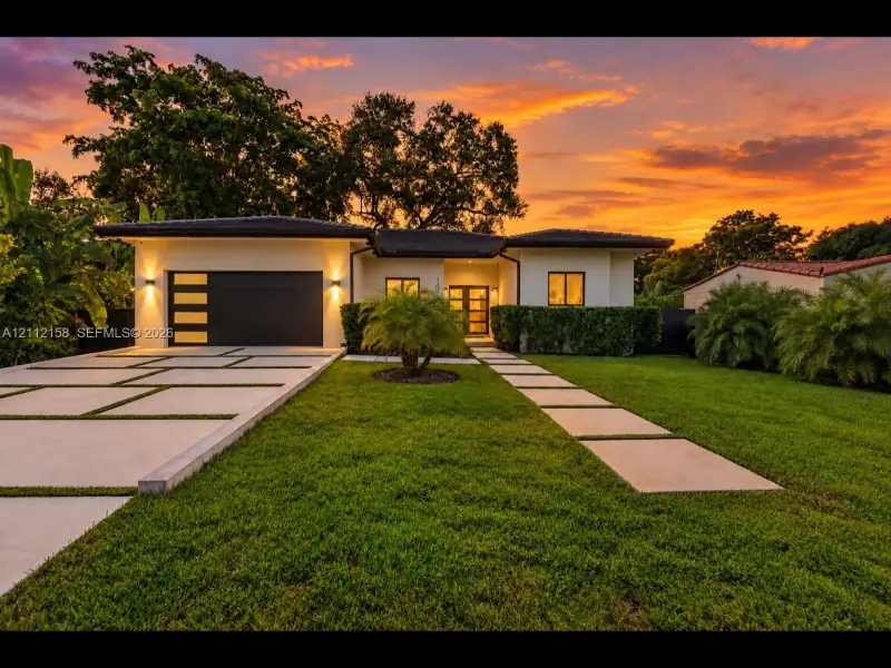 Striking contemporary exterior with a crisp facade, modern multi-panel garage door, and a stylish grass-inlay driveway leading to a recessed entry