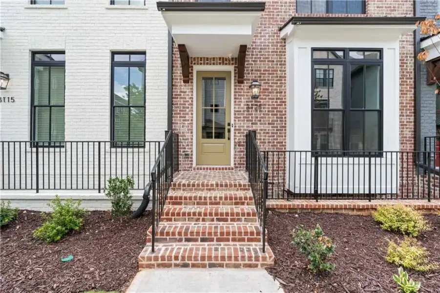Brick and painted brick exterior with a prominent entrance featuring a green door, brick steps, black metal railings, and exterior wall lanterns