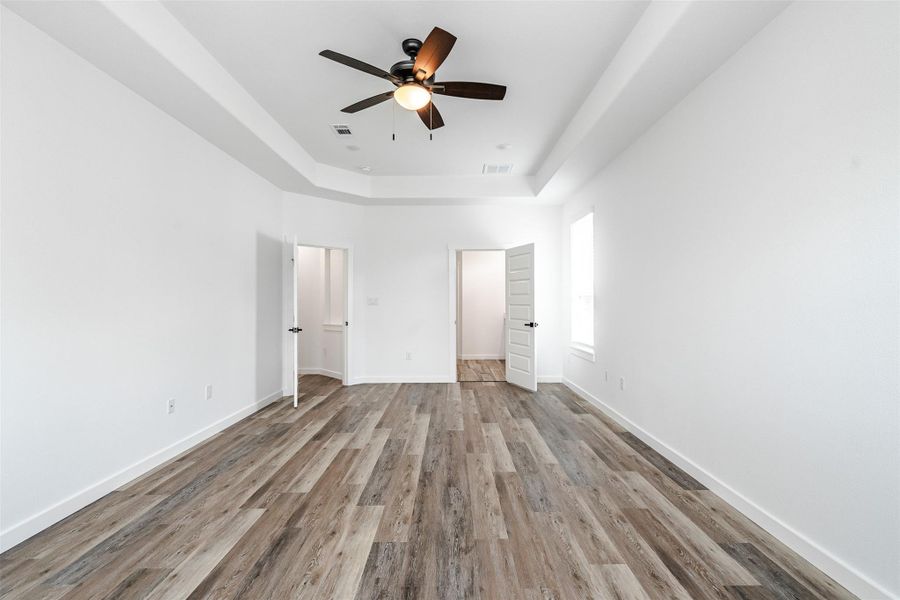 A spacious chamber boasting elegant tray ceilings, plank flooring, and a contemporary ceiling fan. A spacious chamber boasting elegant tray ceilings, plank flooring, and a contemporary ceiling fan.