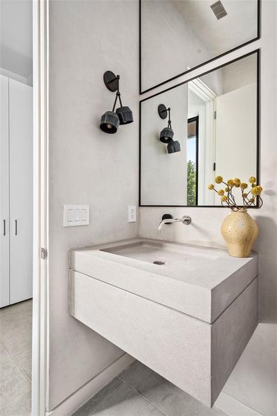 The chic first-floor powder room features elegant plastered walls and a floating custom limestone vanity. The wall-mounted faucet adds to the clean design, while the striking Meteria Designs metal wall sconce provides a touch of modern flair.