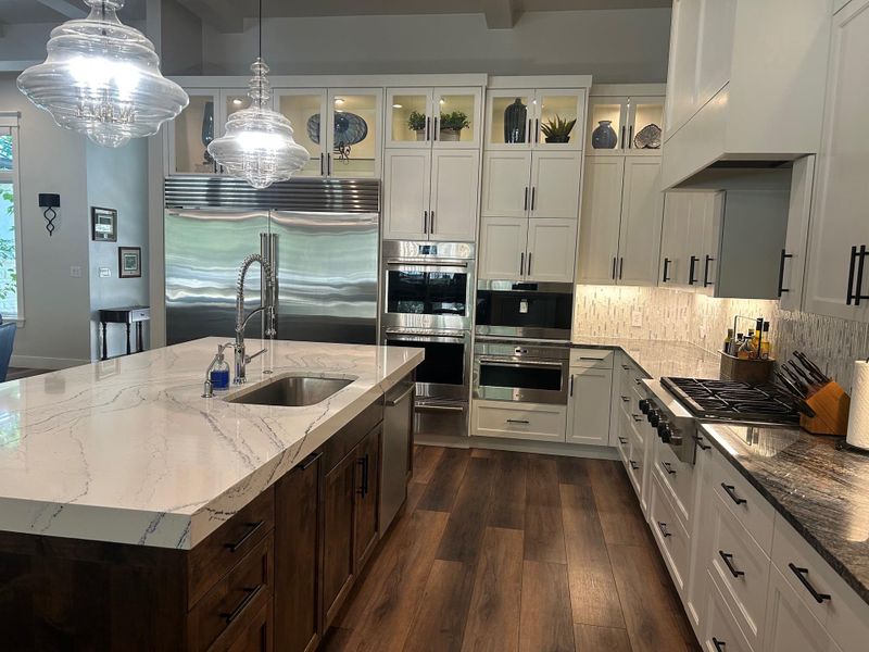 Kitchen with light stone countertops, decorative light fixtures, glass insert cabinets, and an island with sink Kitchen with light stone countertops, decorative light fixtures, glass insert cabinets, and an island with sink