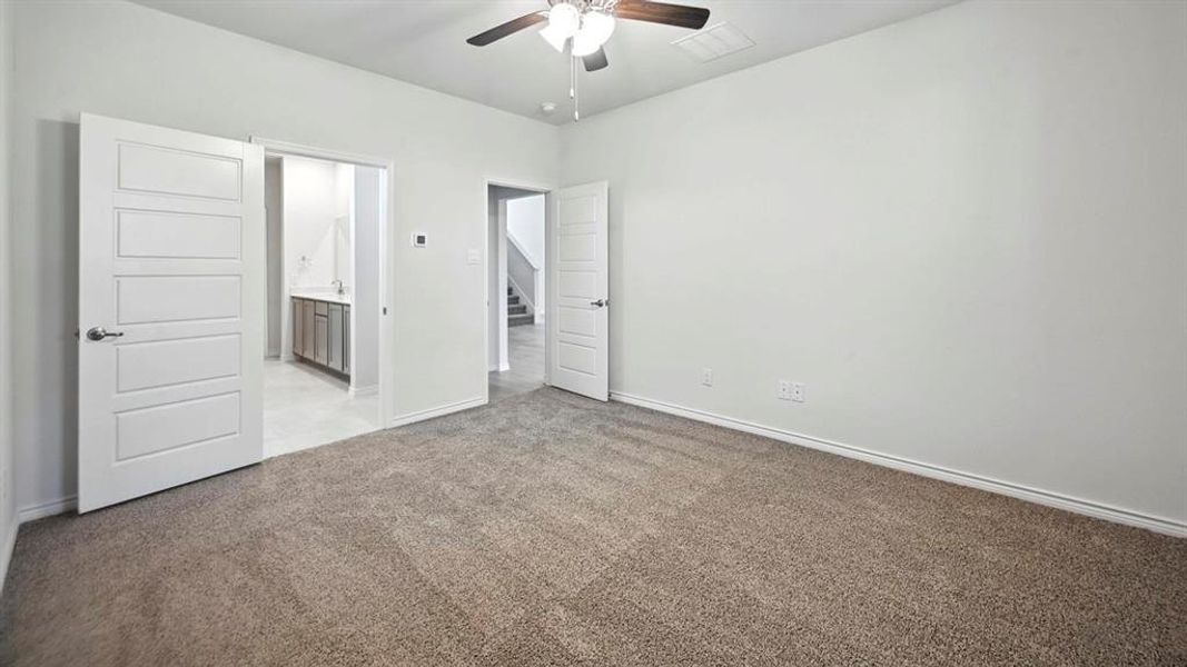 Unfurnished bedroom featuring light carpet, ensuite bath, and ceiling fan