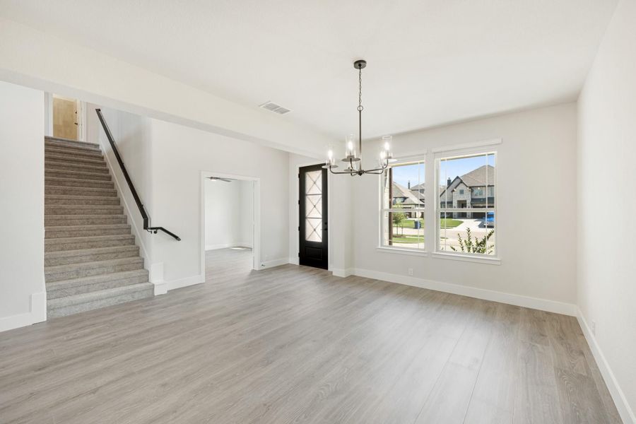 Open living area with light wood floors, chandelier, black front door, and carpeted staircase