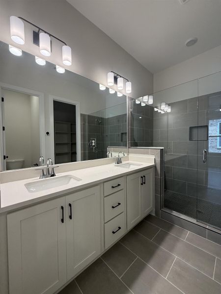 Bathroom with double vanity, a shower stall, dark tile patterned floors, and a walk in closet