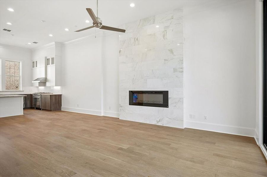 Open-concept living area with wood-finish flooring, a contemporary fireplace with a large-format tile surround, recessed lighting, and a ceiling fan Open-concept living area with wood-finish flooring, a contemporary fireplace with a large-format tile surround, recessed lighting, and a ceiling fan