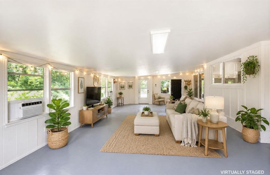Spacious room featuring multiple windows, painted paneling, light-toned flooring, and an air conditioning unit