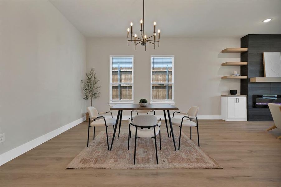 Dining area featuring light wood-style floors, baseboards, a large fireplace, a chandelier, and recessed lighting Dining area featuring light wood-style floors, baseboards, a large fireplace, a chandelier, and recessed lighting