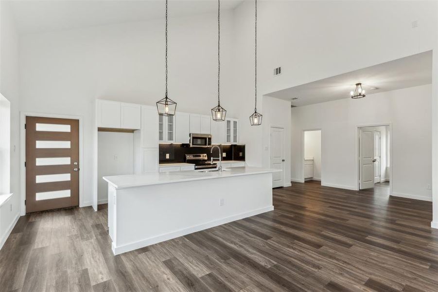 Kitchen with white cabinetry, pendant lighting, stainless steel appliances, and an island with sink