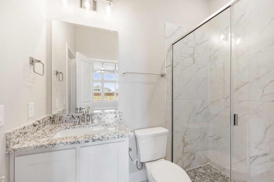 Bathroom with granite vanity, glass walk-in shower with marble tile, and white cabinets