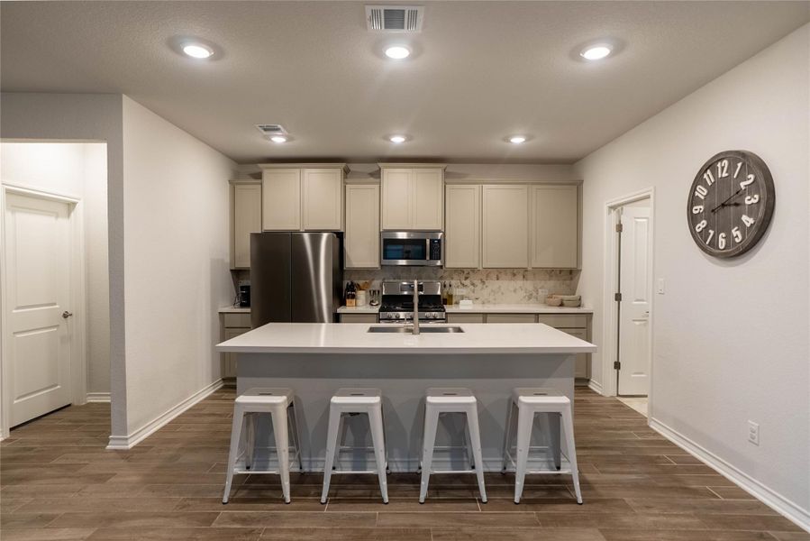 Kitchen featuring appliances with stainless steel finishes, dark wood-style floors, a breakfast bar, decorative backsplash, and a kitchen island with sink Kitchen featuring appliances with stainless steel finishes, dark wood-style floors, a breakfast bar, decorative backsplash, and a kitchen island with sink