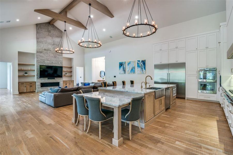 Kitchen featuring white cabinetry, light stone counters, light hardwood / wood-style floors, a large island with sink, and high vaulted ceiling