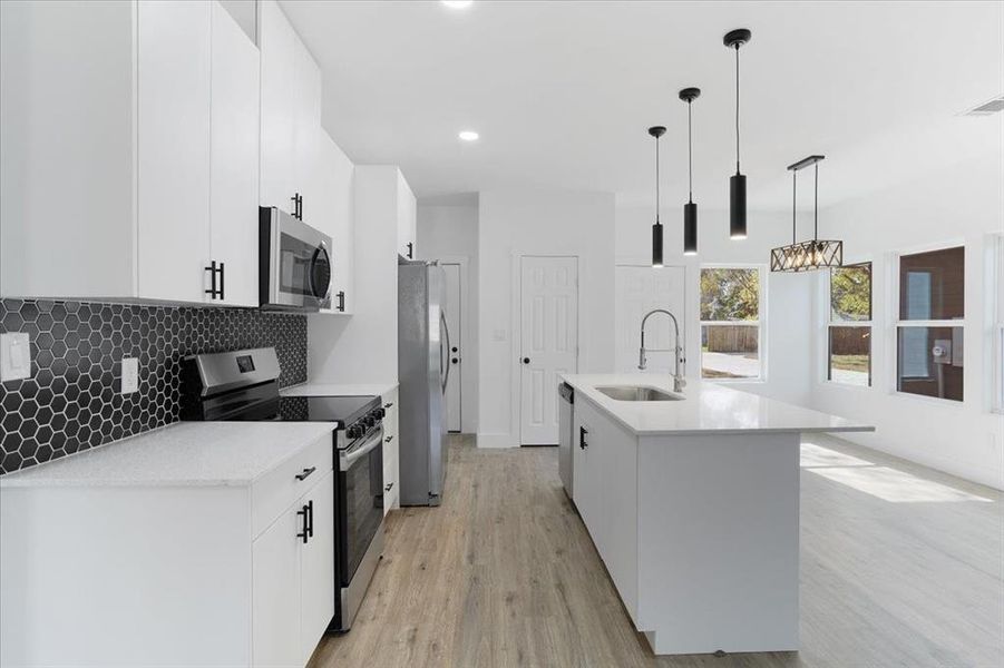 Kitchen with pendant lighting, sink, an island with sink, appliances with stainless steel finishes, and light hardwood / wood-style floors