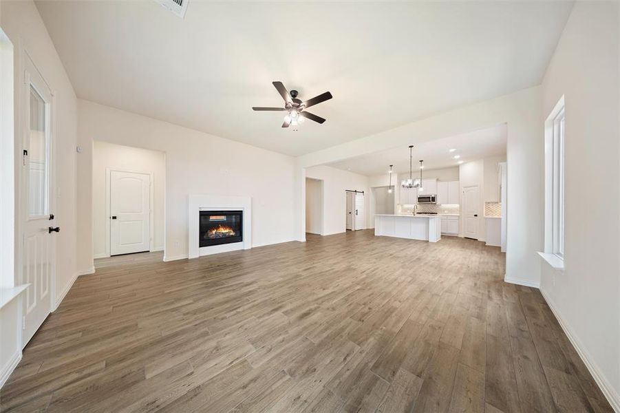 Unfurnished living room with wood finished floors, a glass covered fireplace, ceiling fan, and a chandelier