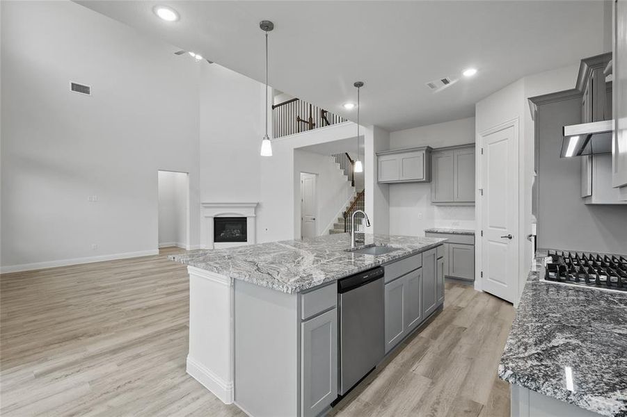 Kitchen featuring gray cabinetry, a sink, appliances with stainless steel finishes, light wood-style flooring, and light stone counters