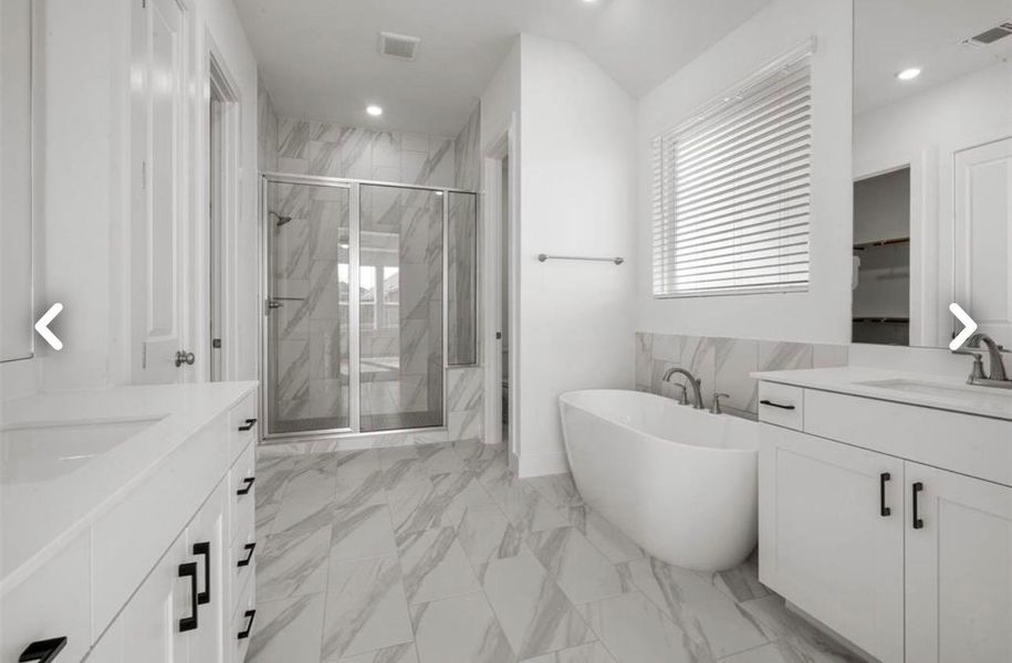 Bathroom featuring two vanities, a marble finish shower, light marble finish flooring, a freestanding tub, and recessed lighting