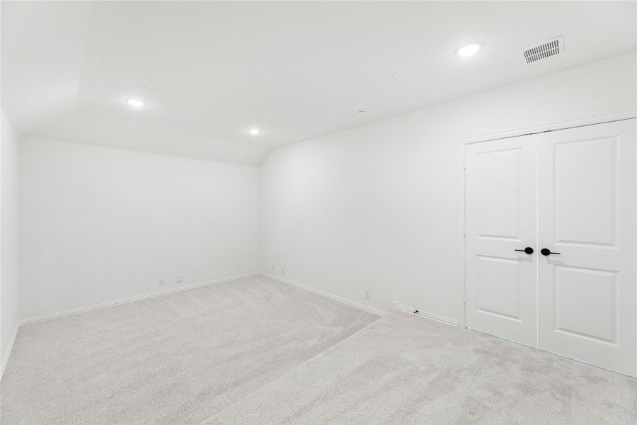 Empty bedroom with white walls, light carpet, recessed lighting, and double closet doors