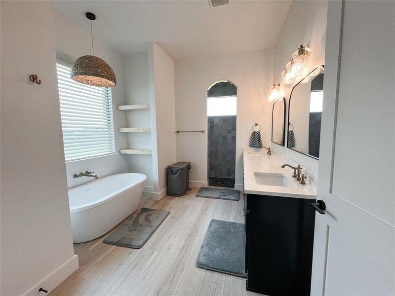 Full bathroom with double vanity, a freestanding tub, light wood-type flooring, and a tile shower