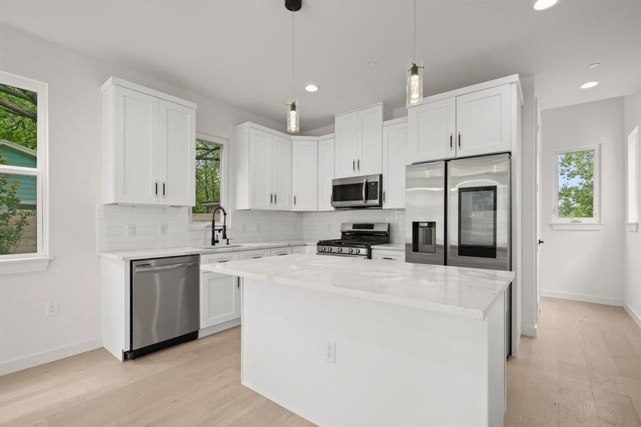 Kitchen with stainless steel appliances, white cabinetry, and light stone countertops