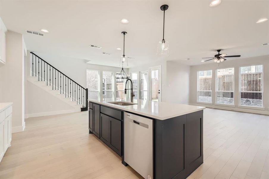 Kitchen with an island with sink, sink, decorative light fixtures, stainless steel dishwasher, and light hardwood / wood-style floors