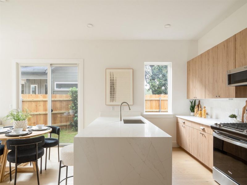 Modern kitchen featuring light wood-finish cabinetry, white stone countertops, and stainless steel appliances